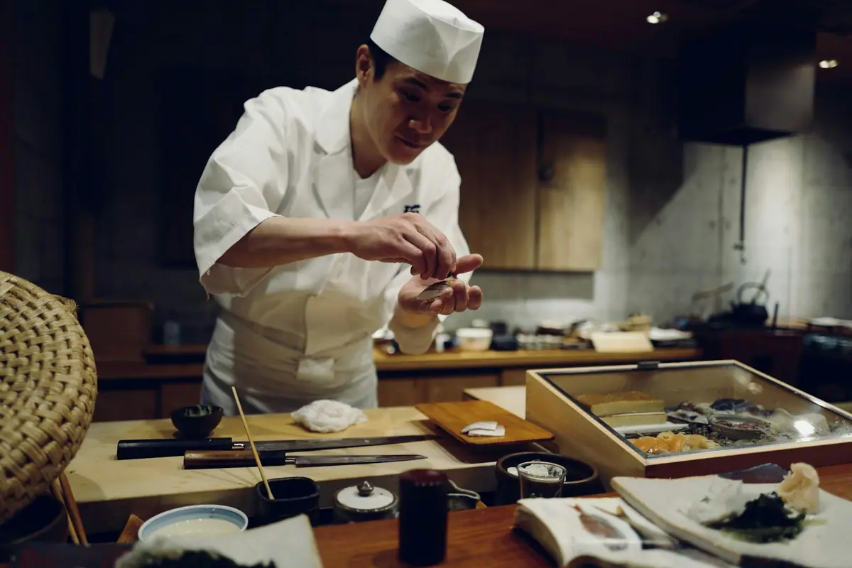 Đầu bếp đội mũ trắng, mặc đồng phục trắng đang làm sushi tại quầy