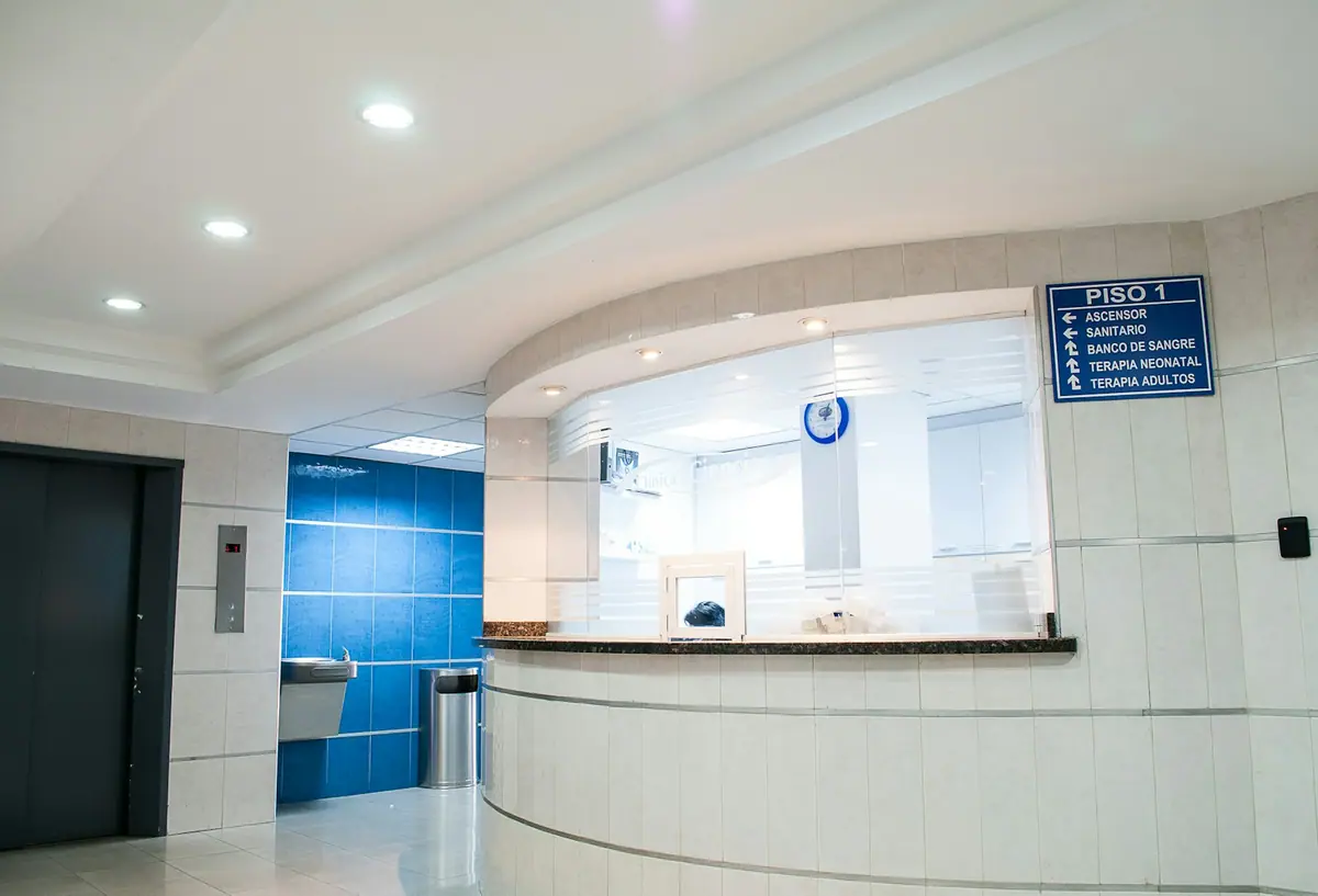 A hospital reception counter with glass windows and a directional sign