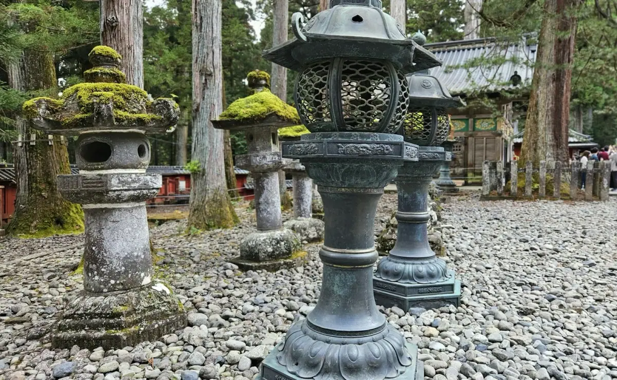 Stone and metal lanterns beneath cedar trees in the grounds of Nikko Toshogu Shrine