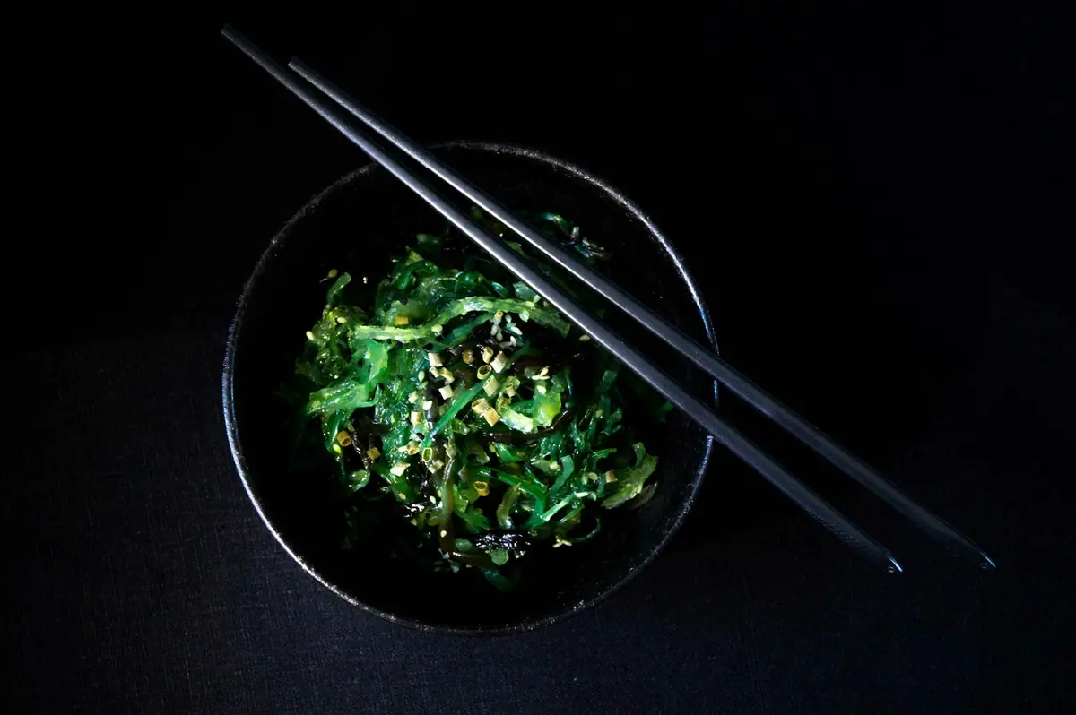 A green vegetable side dish in a small black bowl with chopsticks