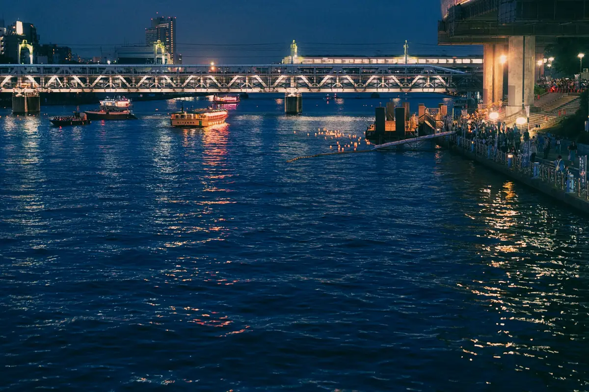 A roofed sightseeing boat on the Sumida River and an illuminated railway bridge in Asakusa at night